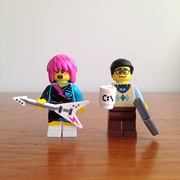 two lego figures standing beside one another holding a guitar