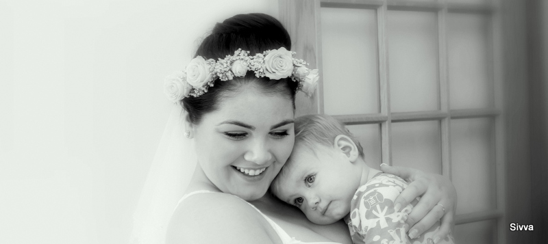 a woman in wedding dress holds her baby in her arms