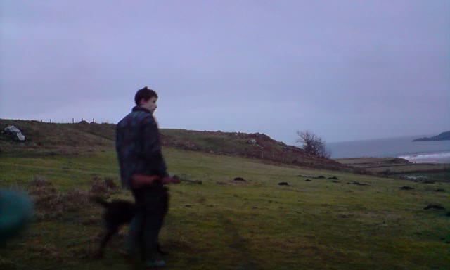 a man standing on top of a lush green hillside next to a dog