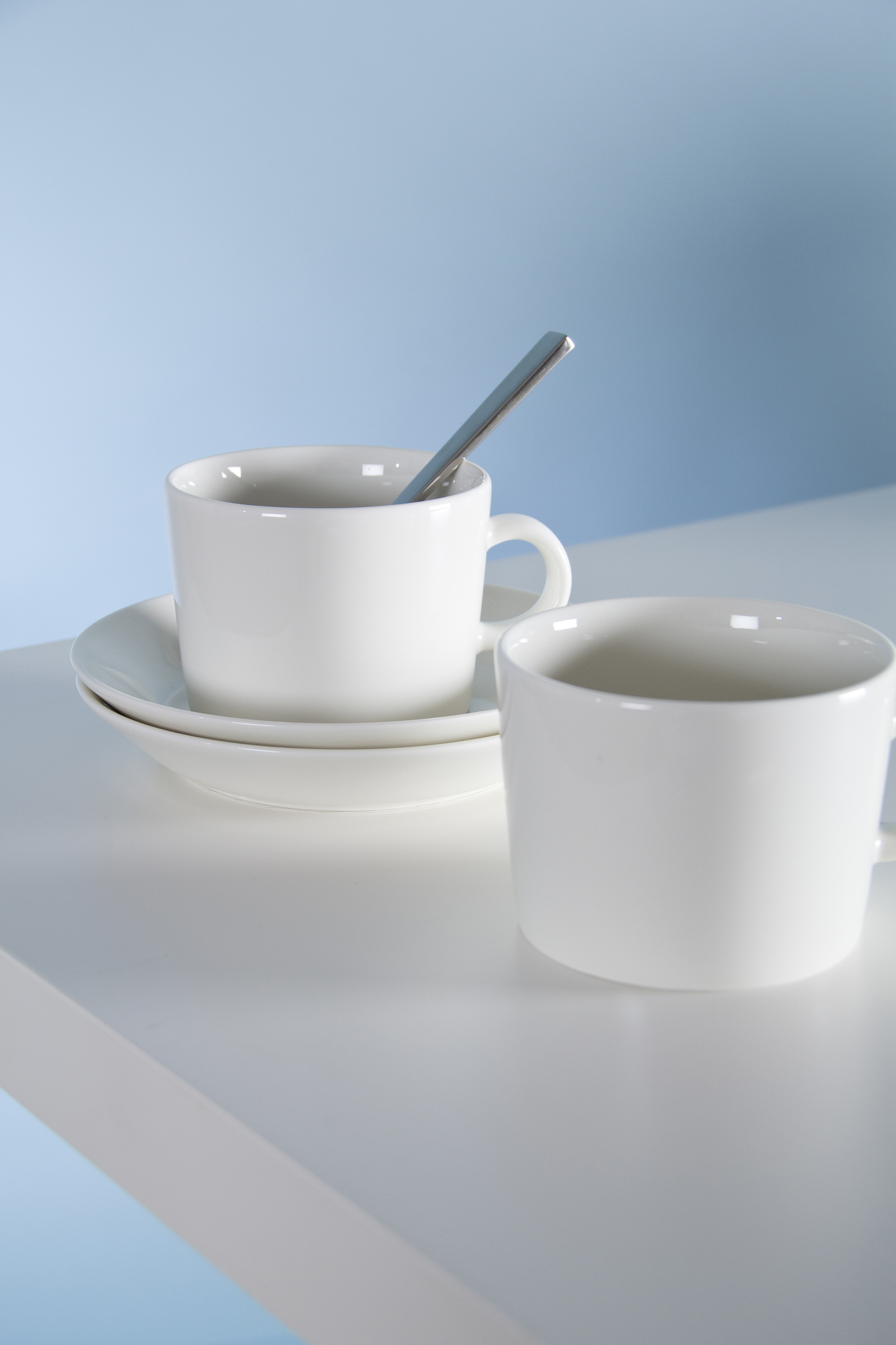 two white cups on saucers with spoons on a table