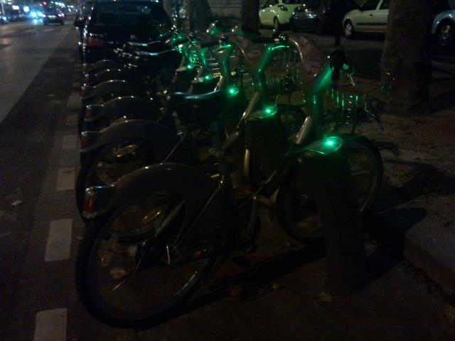 rows of bicycles with green lights on them sitting in front of trees