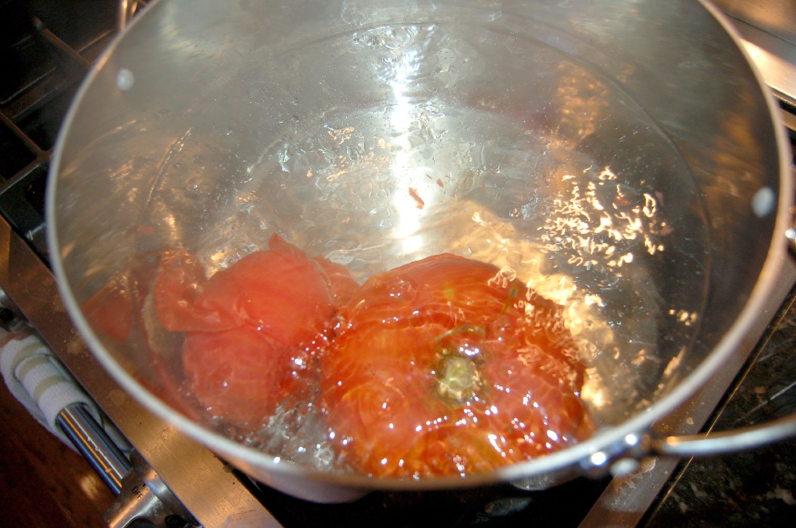 some tomatoes are in a metal bowl on the stove