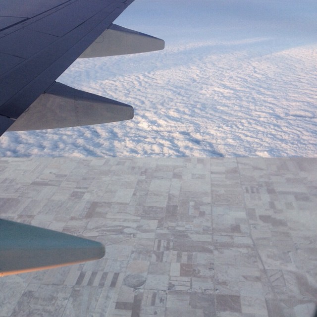 a view from the wing of an airplane looking at clouds and land