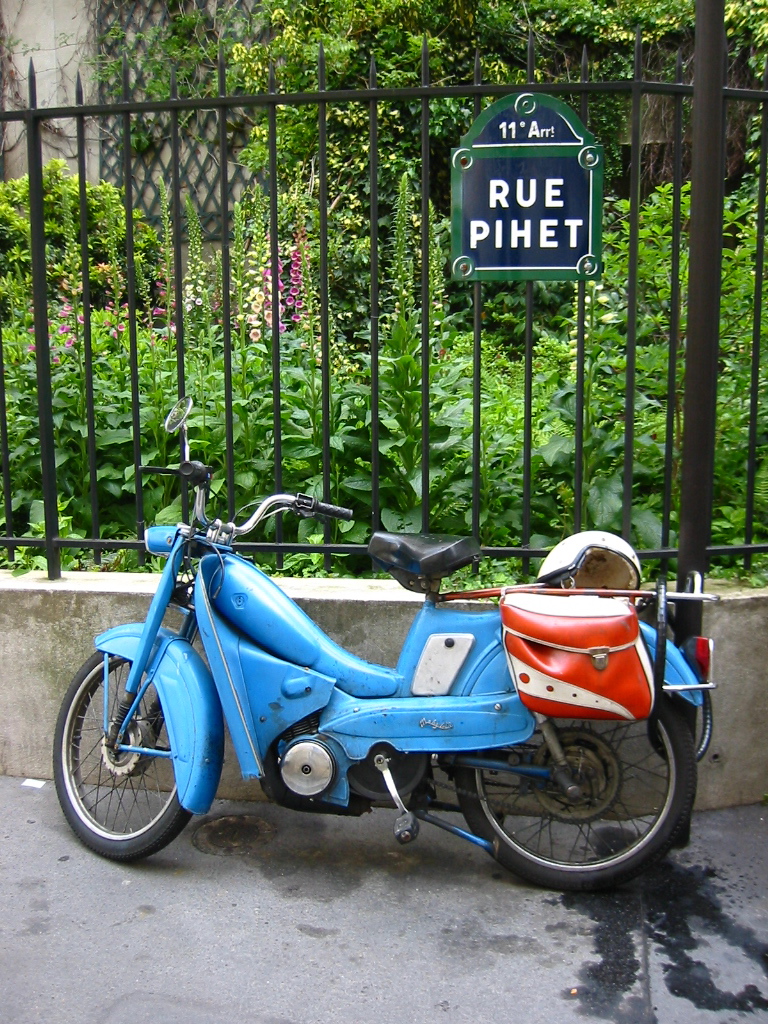 a blue moped parked next to a fence