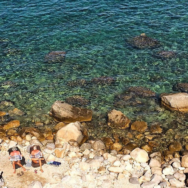 a man and a woman sitting on the beach near water