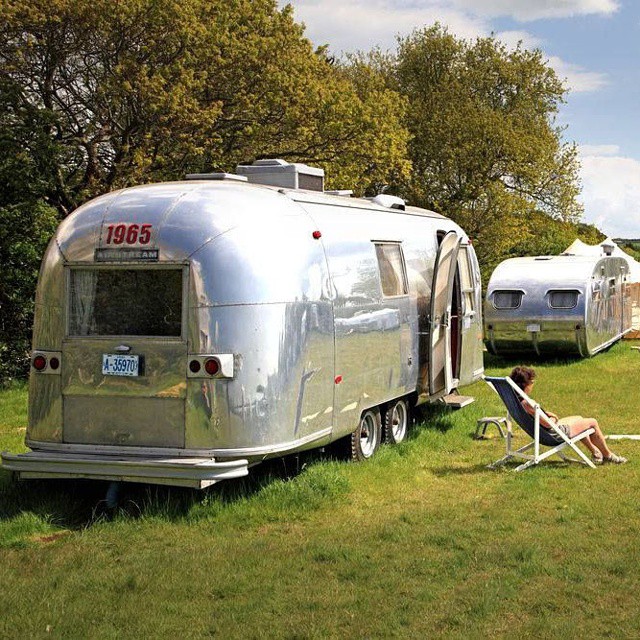 a couple of silver trailer campers sitting on a green field