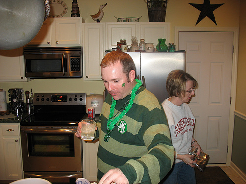 a man with a green sweater and a st patricks necklace pours beer