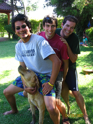 three men pose with a dog in the grass
