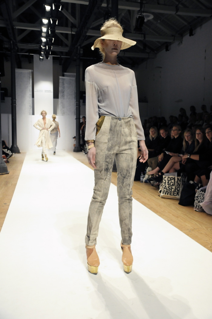 a model wears an outfit while standing on the catwalk