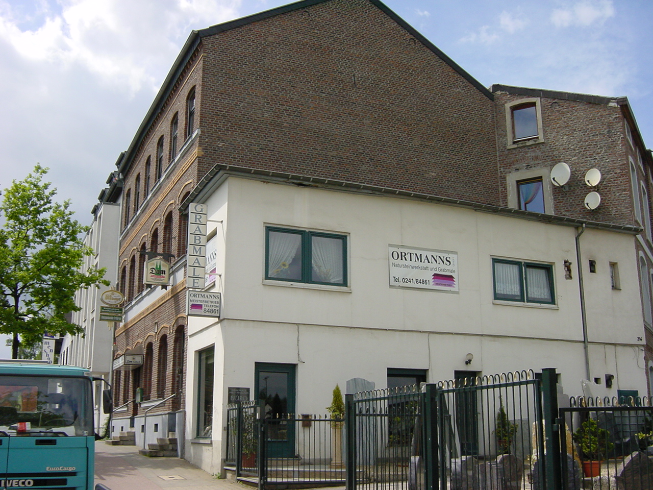 the front of a white building with a black gate and large brown brick building next to it