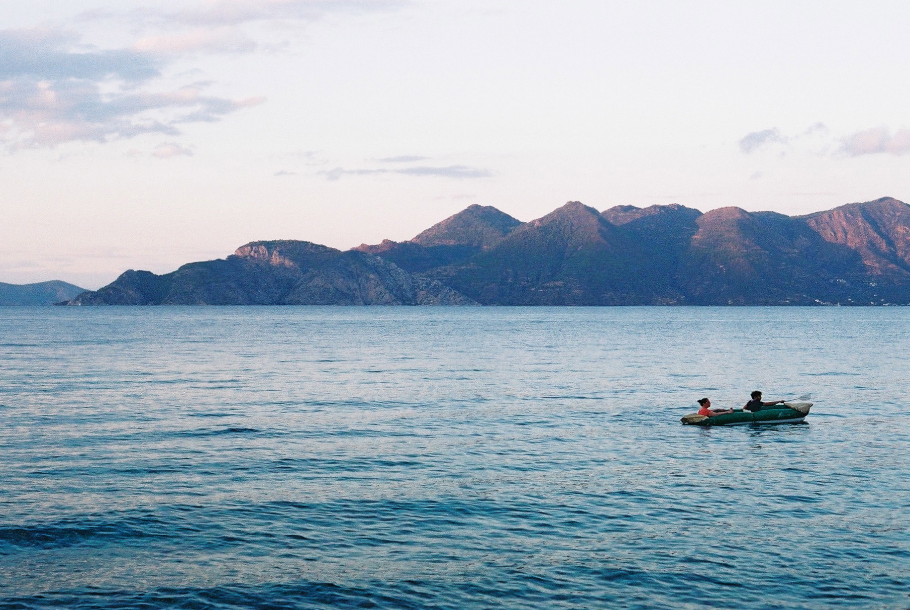 two people in a small boat with mountains behind them