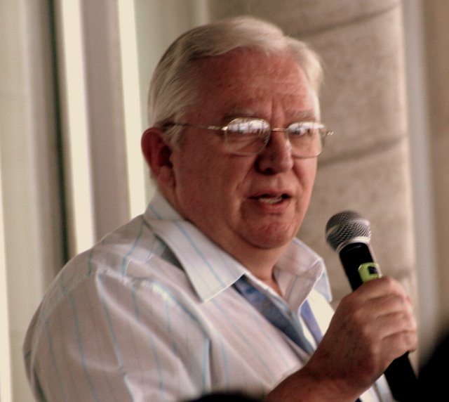 man in glasses speaking into microphone while standing near crowd