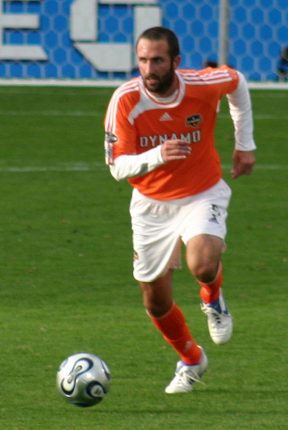 a man in an orange shirt kicking a soccer ball