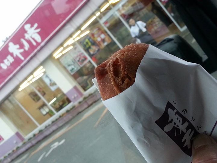 the hand holding a piece of food in front of a store