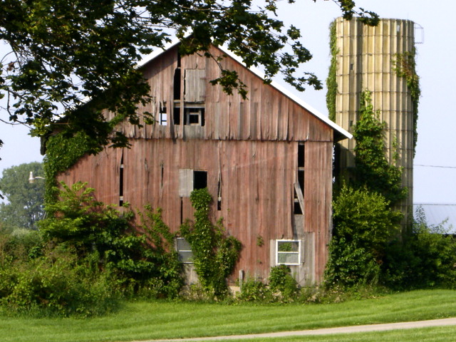 an old barn next to an abandoned silo in rural area