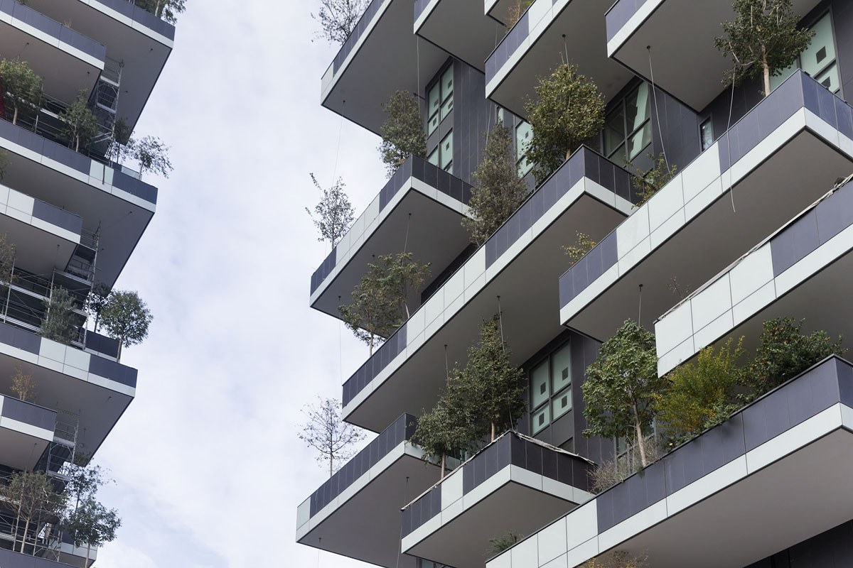a tall gray building with trees and plants on each balcony
