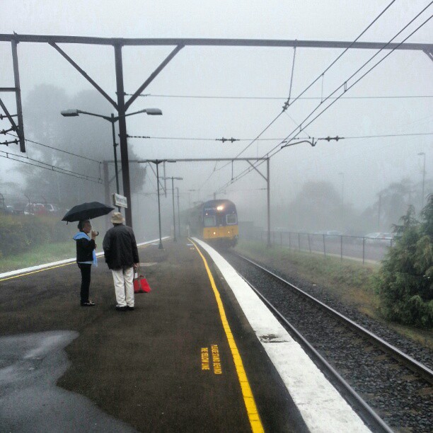 two people walking down a railroad platform with an umbrella