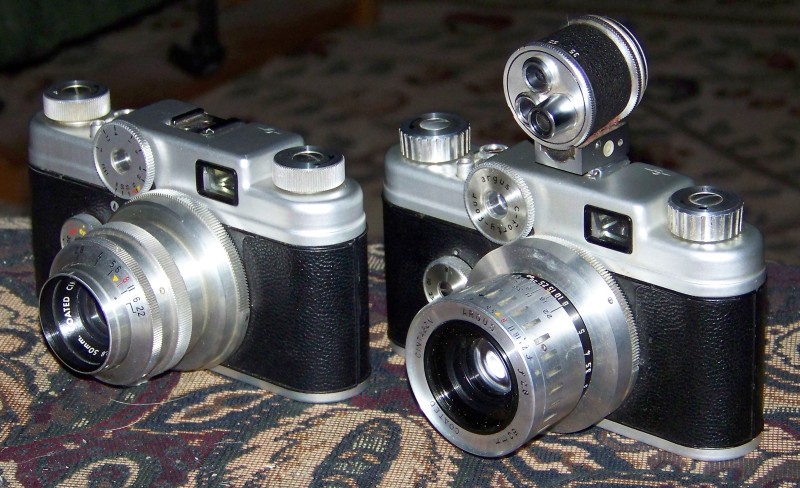 two silver vintage cameras sitting on a rug