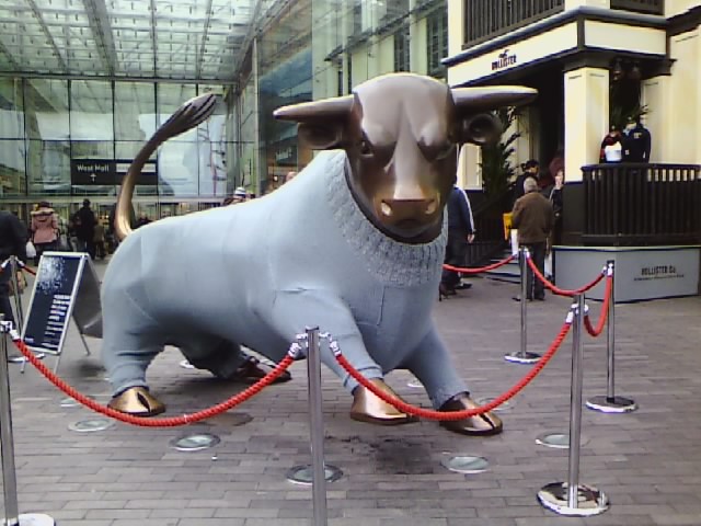 a very big metal bull statue with a rope on a city street