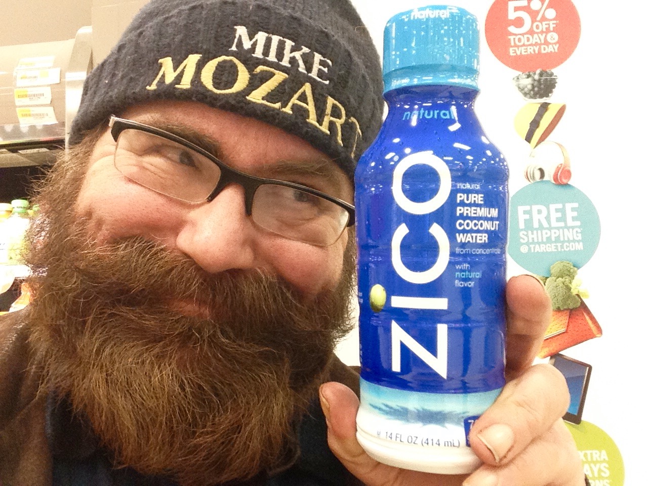 a man with glasses holds up a bottled blue drink