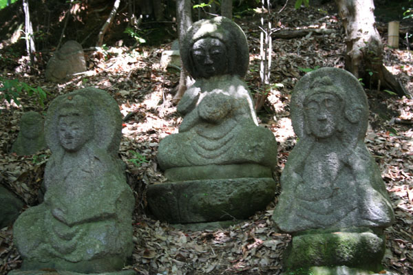 several stone sculptures in the woods with lots of leaves