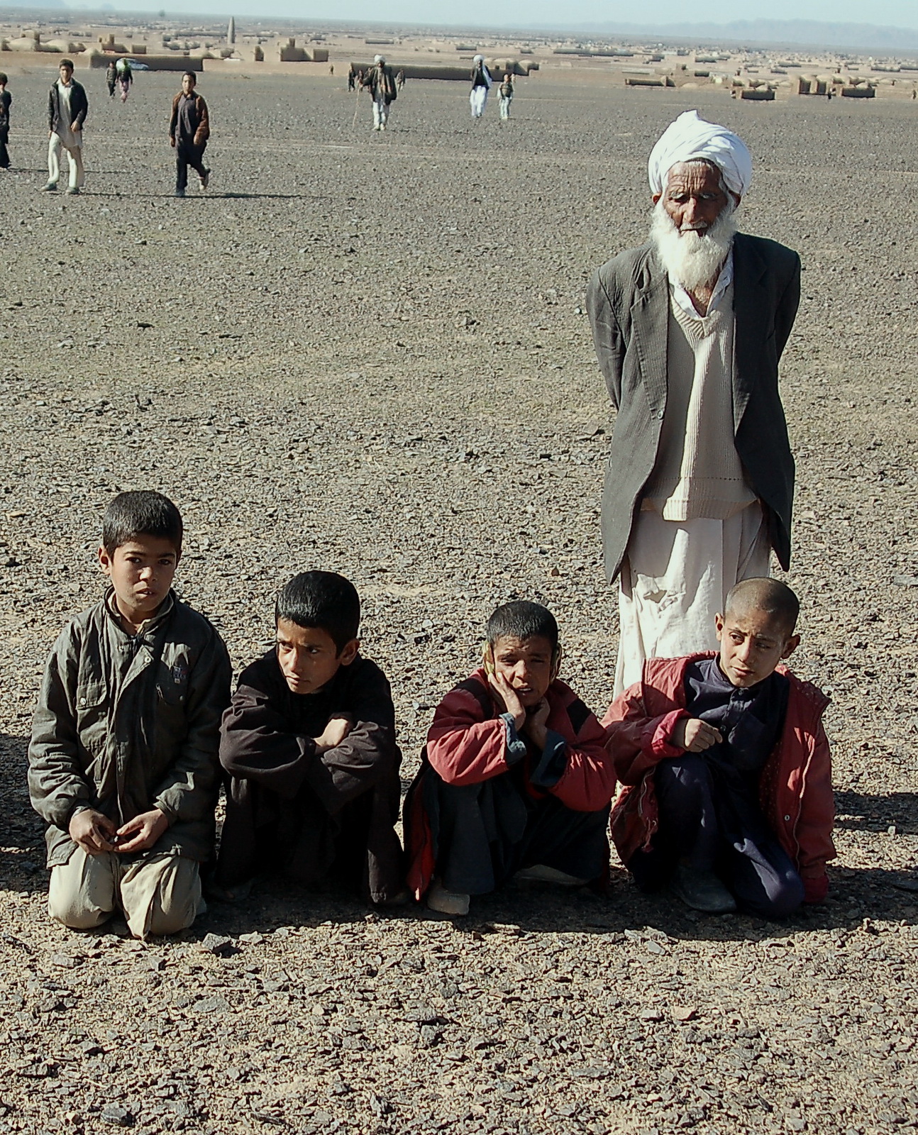 several children standing in the desert with a large figure of an old man