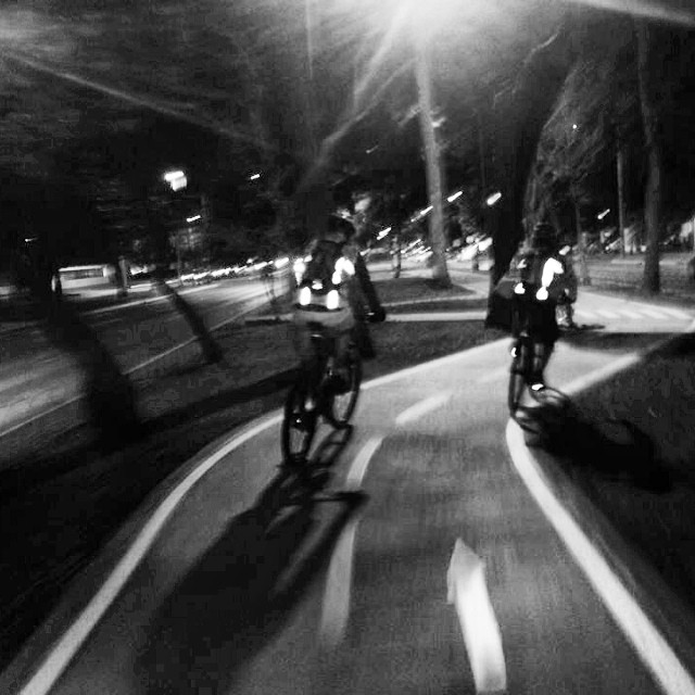 three men on bicycles ride down the road at night