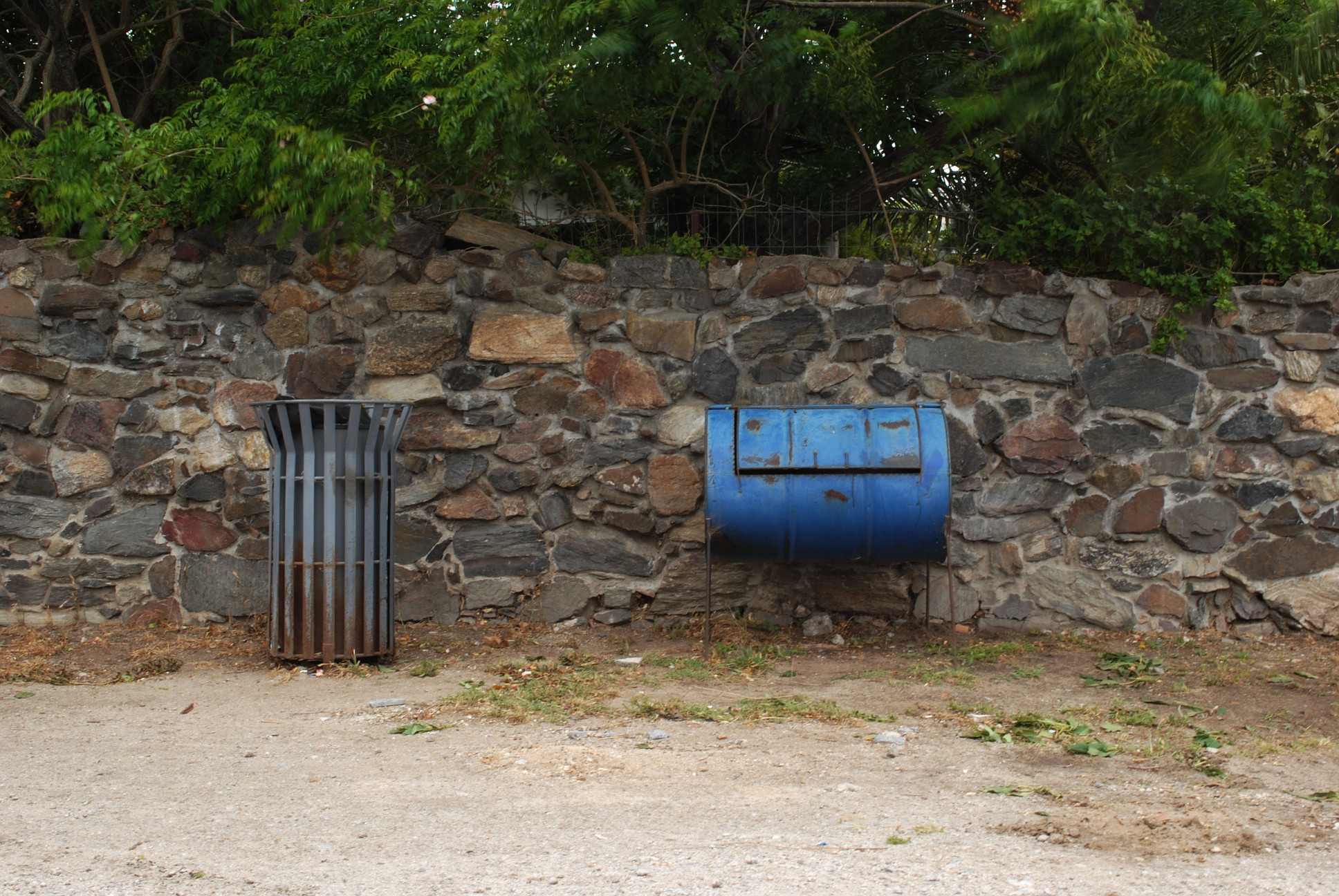 a wall made of a bunch of stones with a blue trash can in front of it