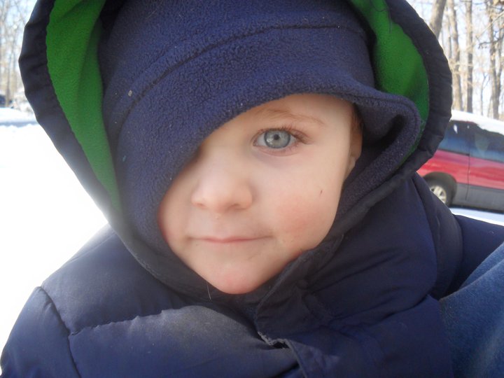 little boy in a blue jacket in the snow with an odd shaped face