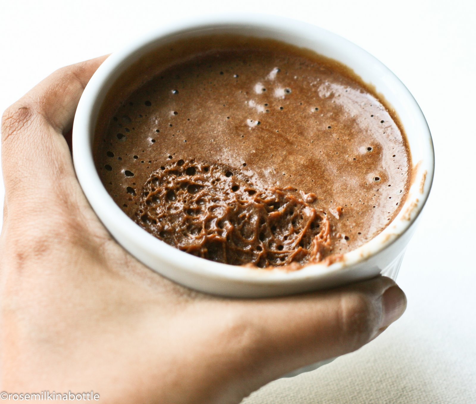 a hand holds a coffee cup with chocolate substance on it