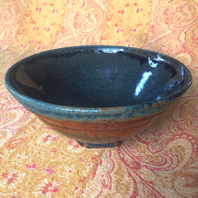 a brown and green bowl on a colorful cloth