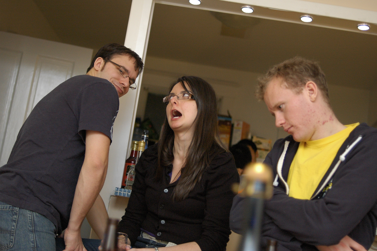 three people standing around a cake in the kitchen