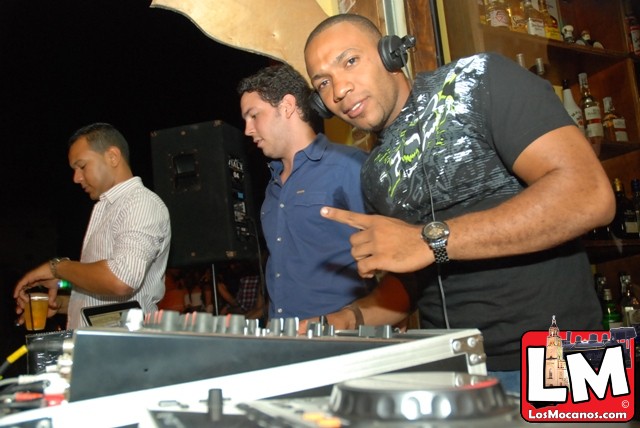 two men standing behind a dj in front of a crowd