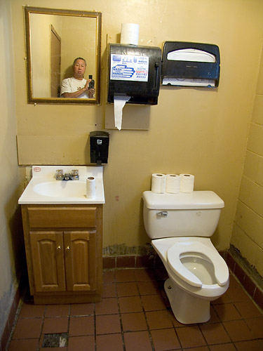 a man in a bathroom reflected in a mirror next to a toilet