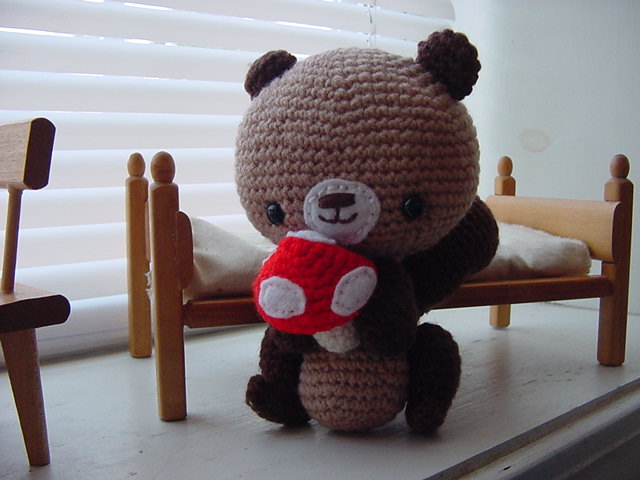 a crocheted teddy bear sitting with a red cup