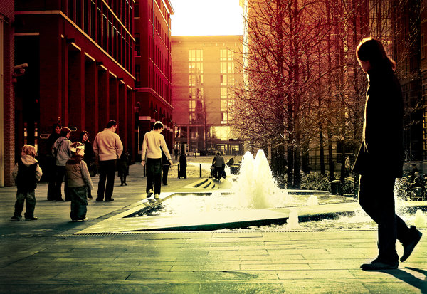 a person stands next to a fountain on the corner of a city street