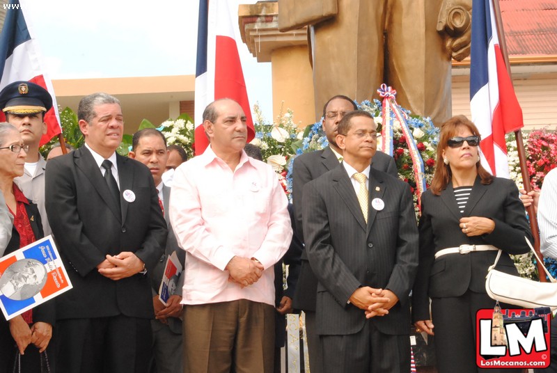 many people stand together at a ceremony in front of flags