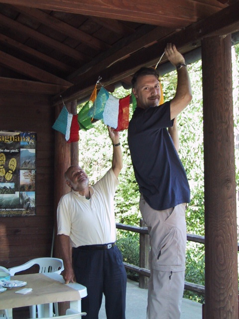 a man hanging up a cloth on a clothes line next to another man in a blue shirt