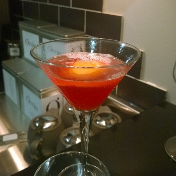 a small red cocktail sits in the middle of a wine glass on a counter