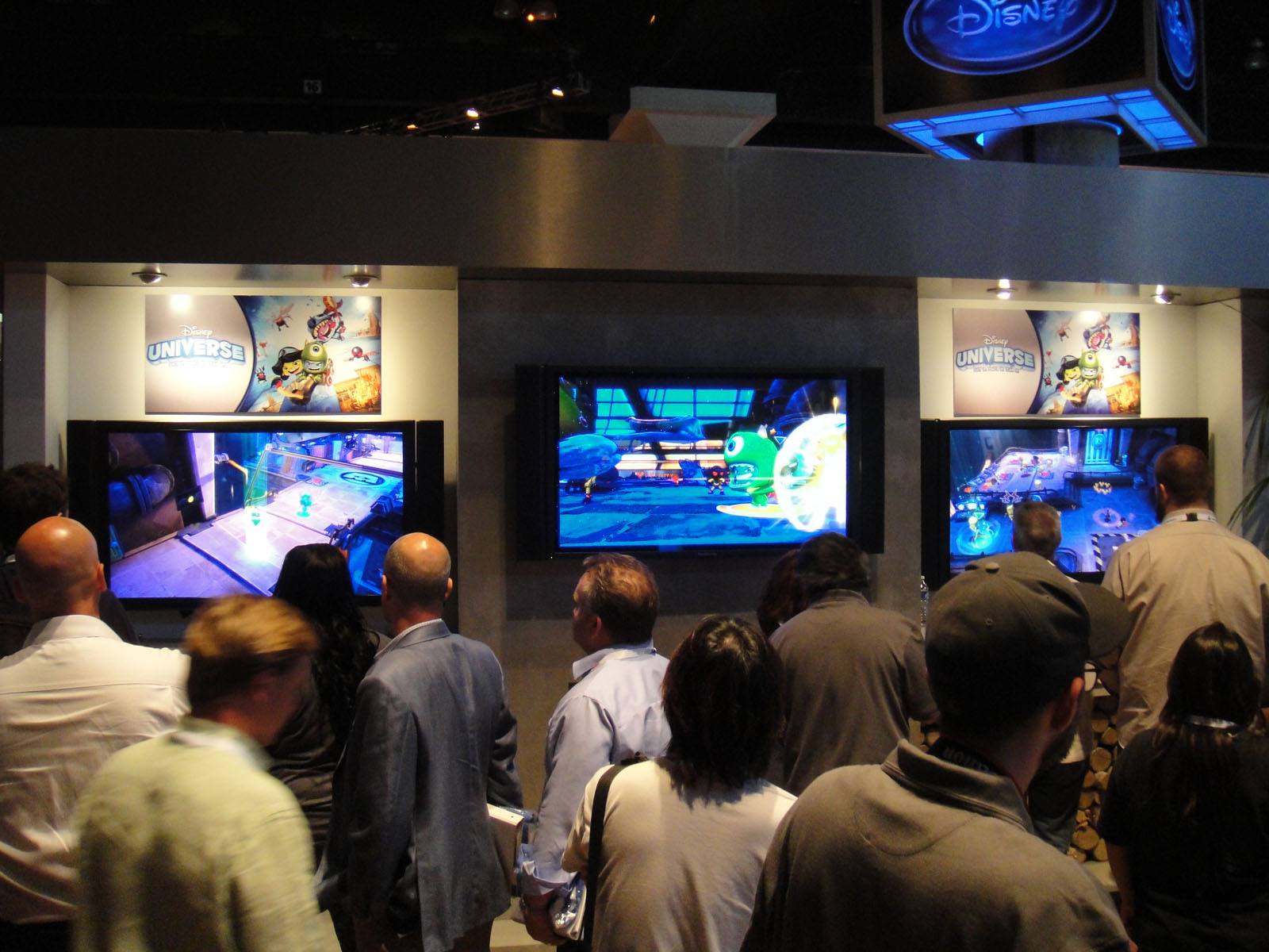 several people standing up in front of three large television screens