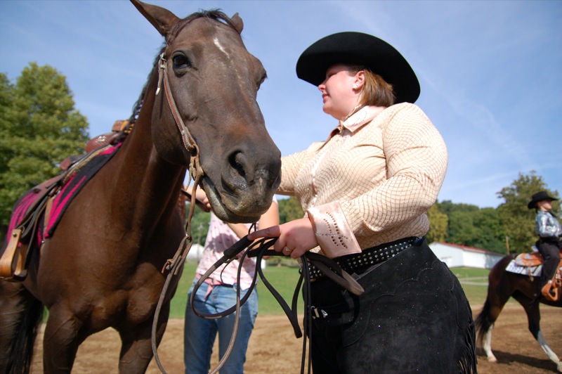 woman in white sweater, black hat and jeans on horseback