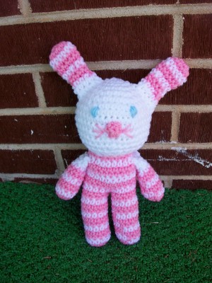 a knitted pink and white rabbit toy sitting by a brick wall