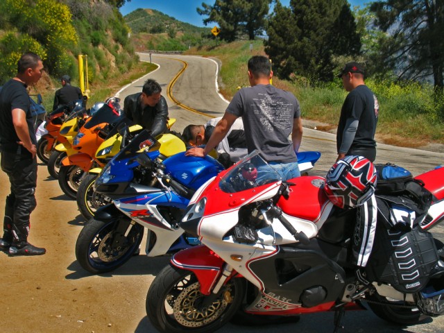 five men talk to two motorcycles on the side of a road