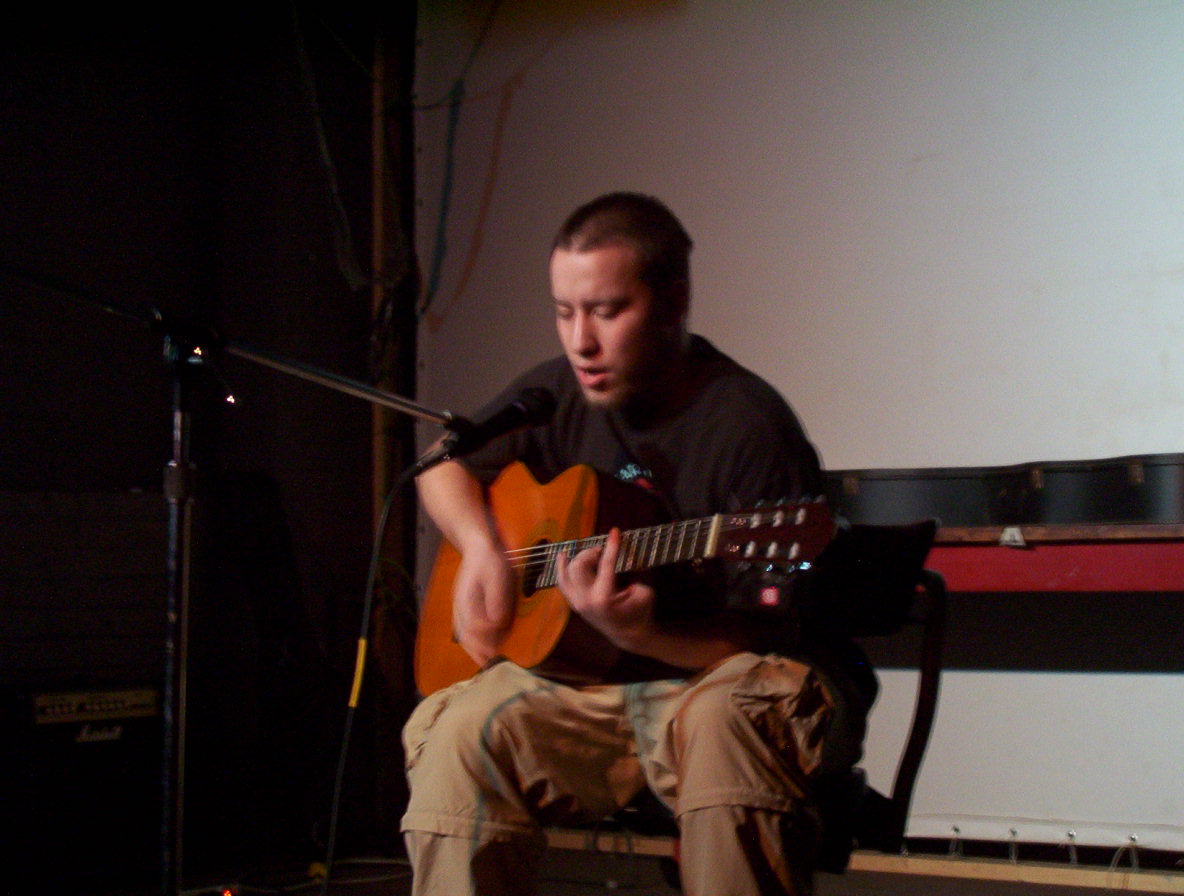 man in black shirt playing guitar by a microphone