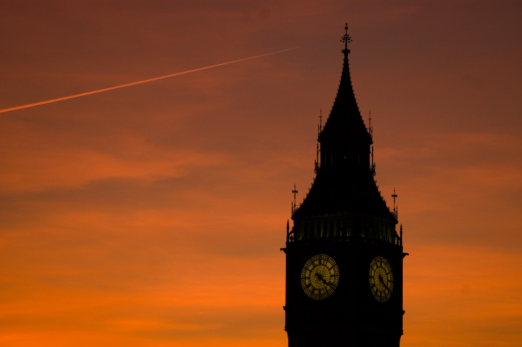 a clock tower with two roman numerals is silhouetted against an orange sky