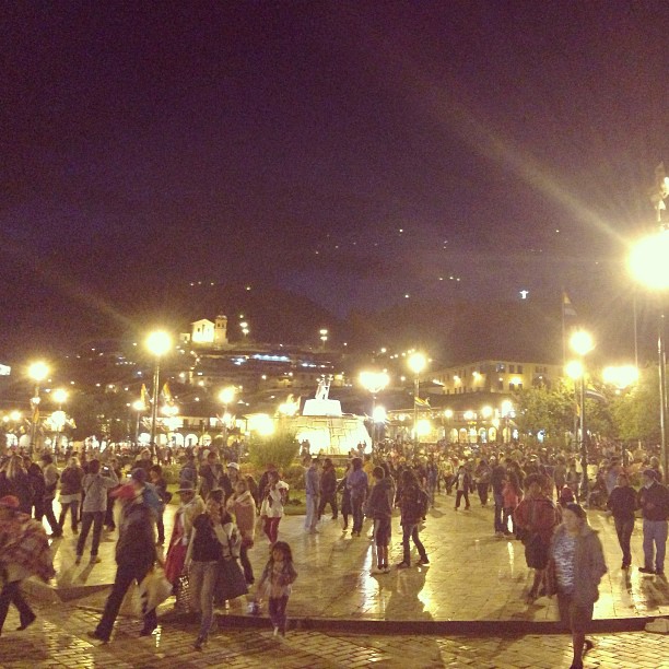 people walking through a plaza at night in front of lit up buildings