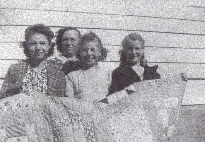 black and white pograph of four women with quilts on a house porch