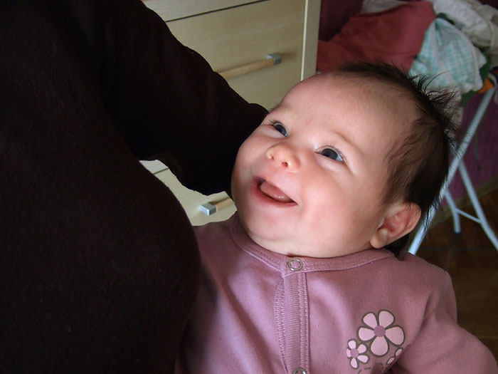 a smiling baby sits between a persons hand