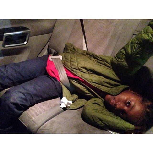 a person wearing blue jeans and a green jacket sleeping in a car