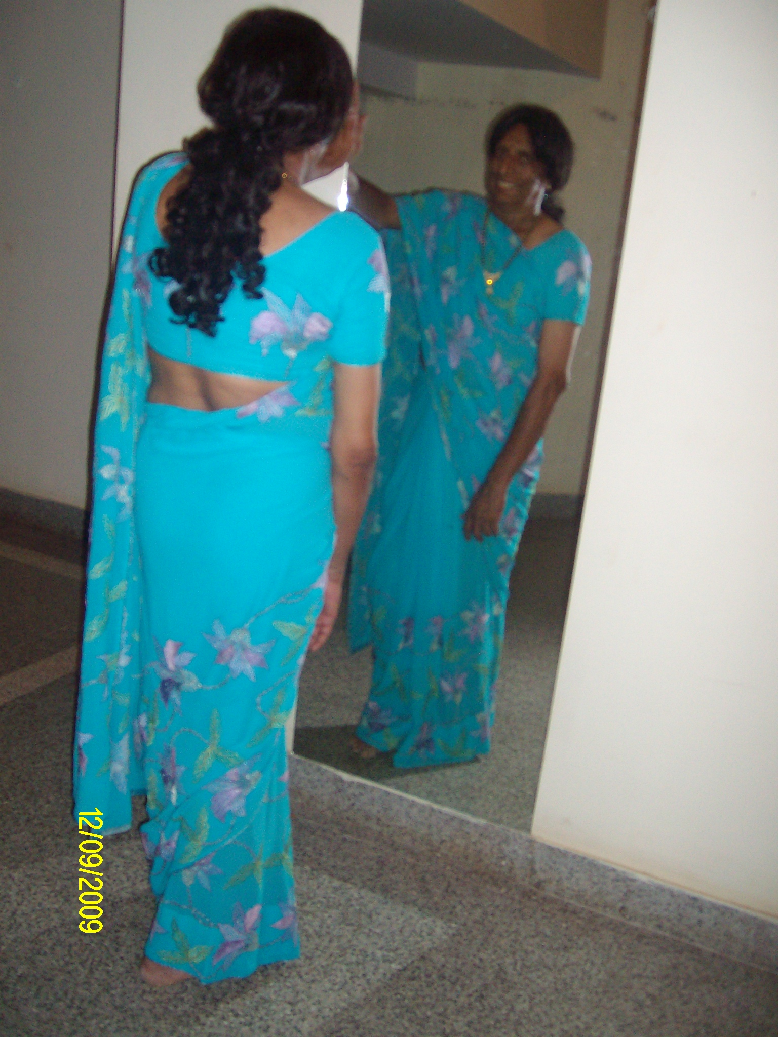 two women standing in a hallway and wearing blue sari